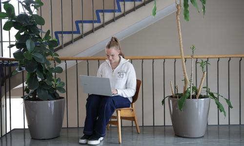 A student sitting in Hanken's corridor working on a laptop