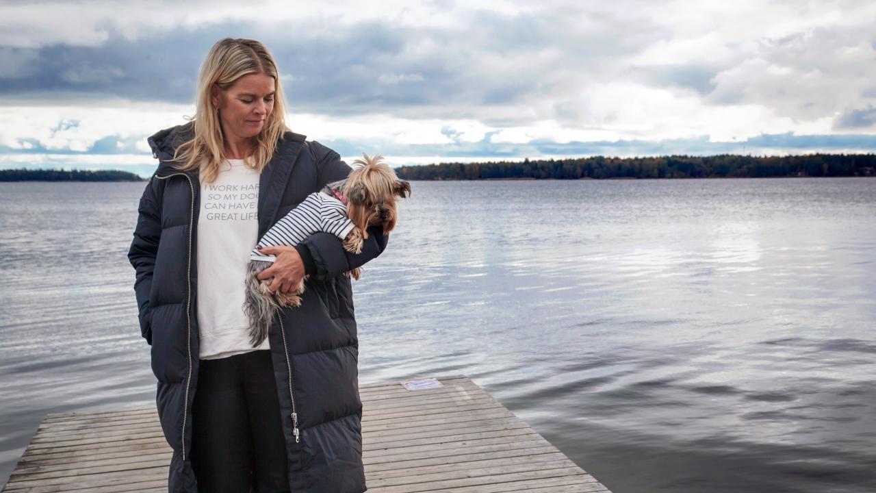 Ullica Hansson står på en brygga och ser på sin hund som hon har i famnen.