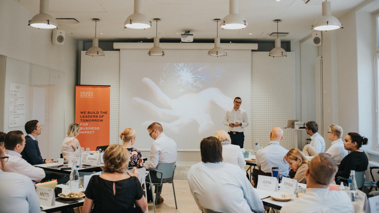 En person står och föreläser framför en grupp människor