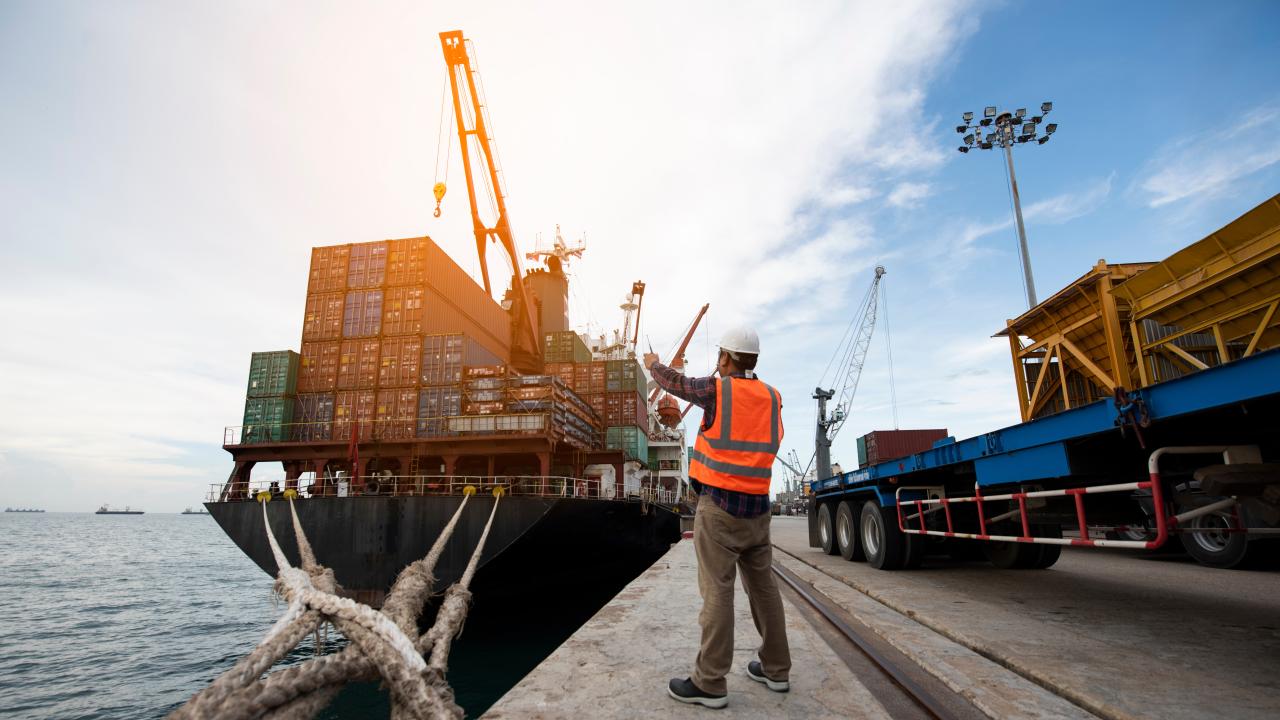 A man on a loading dock directing a fully loaded ship.