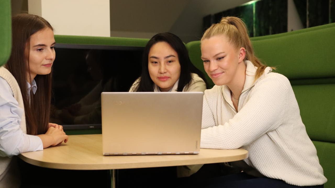 Tre studenter sitter samlade runt en dator