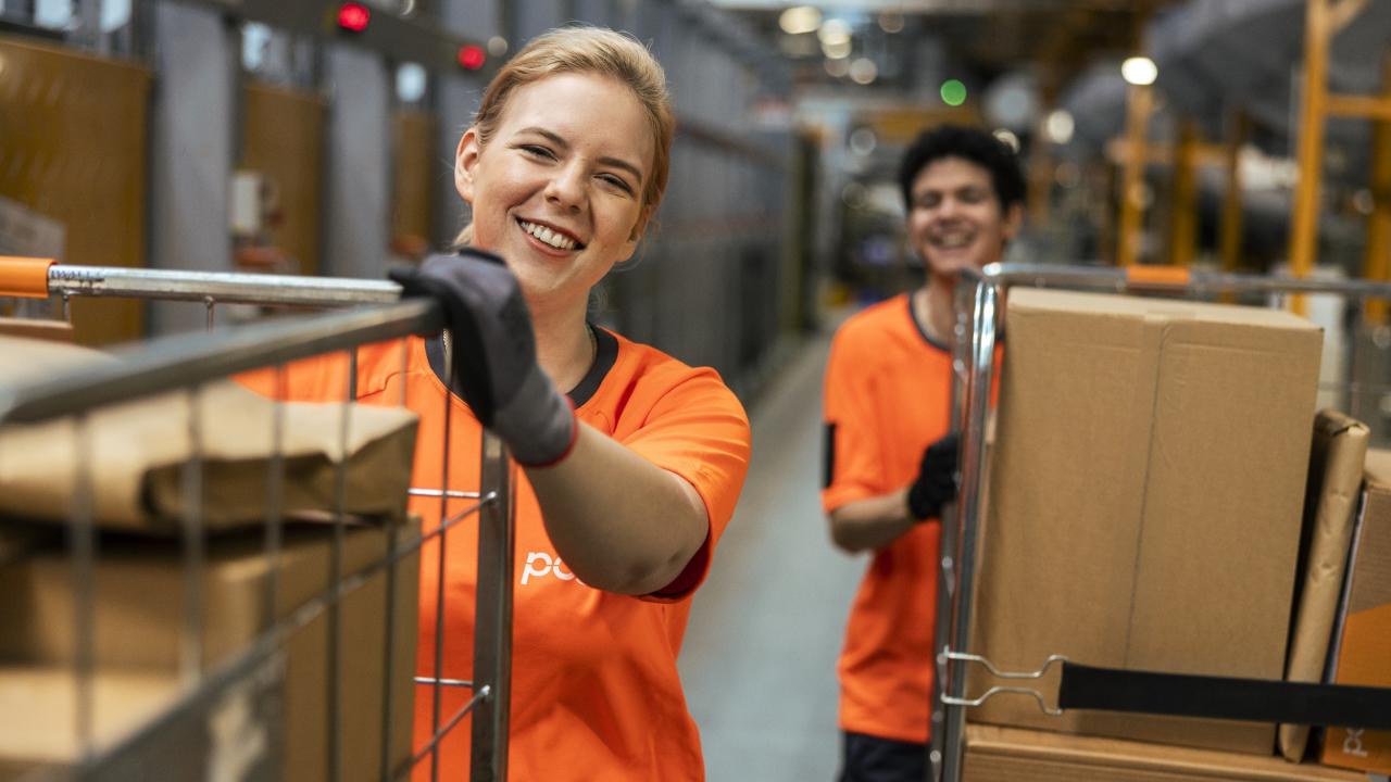 Två personer som transporterar paket i en lagerlokal.