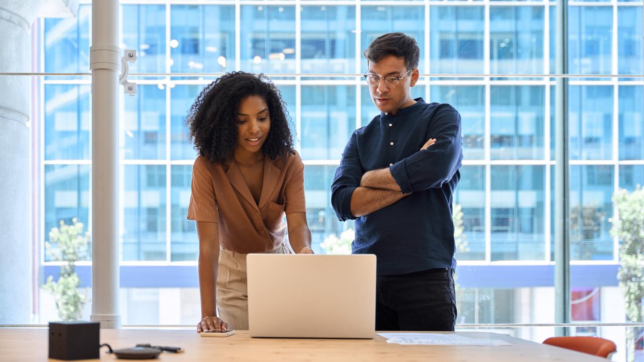A woman and a man standing in front of a computer in an office, talking to each other.
