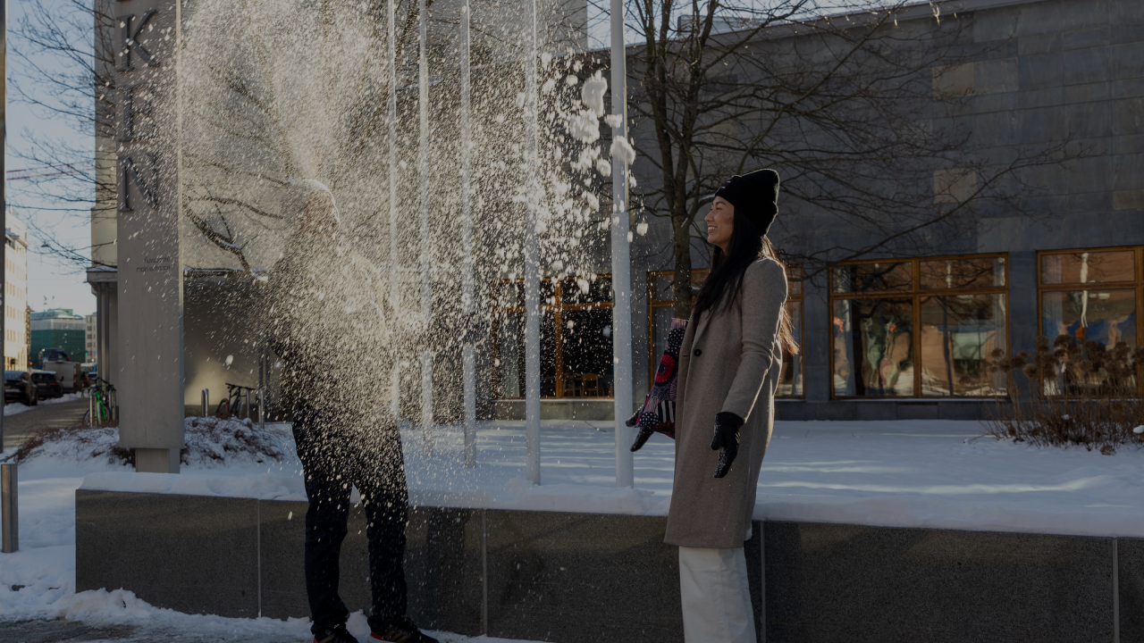 Two students outside Hanken throwing snow in the air