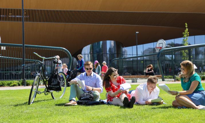 Studenter sitter på en gräsmatta framför Ode-biblioteket