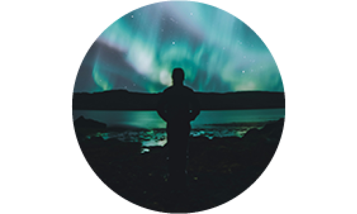 A silhouette of a person standing in front of northern lights