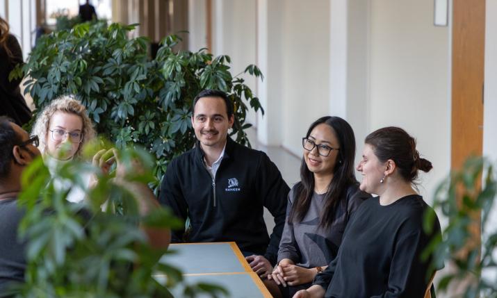 Five PhD students sitting at a table with plants in the background