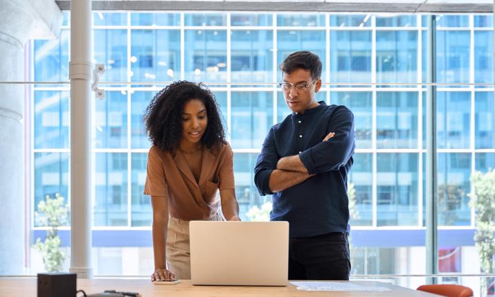 A woman and a man standing in front of a computer in an office, talking to each other.