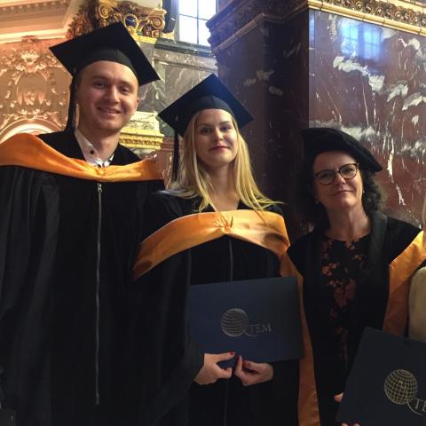 Två studenter och en professor med högtidlig klädsel.