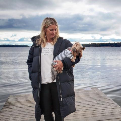 Ullica Hansson står på en brygga och ser på sin hund som hon har i famnen.