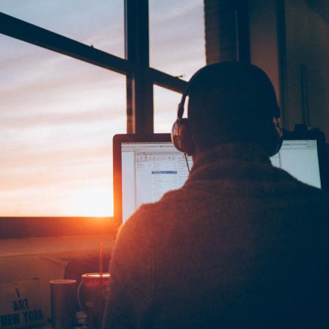 Människa vid en dator inomhus, solnedång syns i fönstret