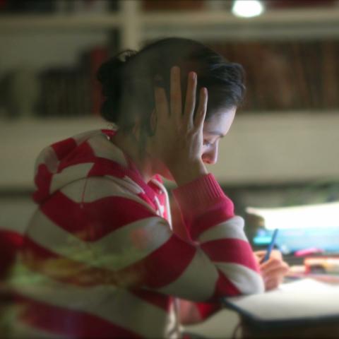 Människa sitter och skriver vid dator och lutar huvudet i handen