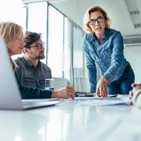 Kvinna som pratar till en grupp människor vid ett mötesbord