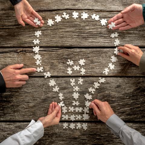 Händer som lägger ett pussel i form av en glödlampa