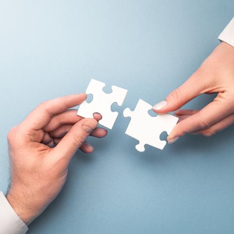 Två händer som sträcker sig mot varandra och håller i pusselbitar