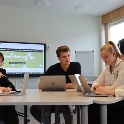 Några studerande sitter vid ett bord och jobbar på sina datorer.