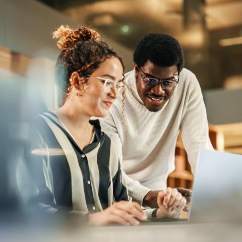 Two people in front of a computer in an office setting.