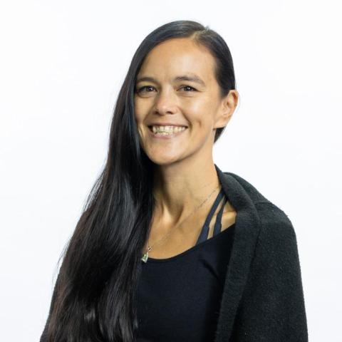 A photo of Fon, smiling. Fon is mixed Asian/White. They have long black hair parted on the left and light brown skin.